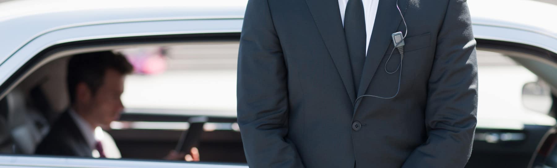 Bodyguard im Anzug mit Ohrhörer vor dem Fahrzeug der Schutzperson