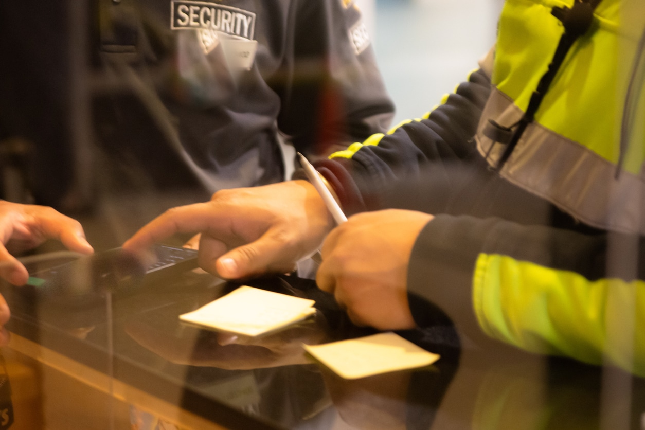 Wachperson am Empfang prüft die Unterlagen eines Besuchers